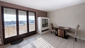 A room with a balcony, a dining table with chairs, and a cabinet. - Le Cosy Gaillard, 3 stars. City view and private parking space. (Brive-la-Gaillarde)