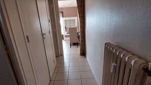 A hallway with a radiator, a door, and a view into a room with a table and chairs. - Le Cosy Gaillard, 3 stars. City view and private parking space. (Brive-la-Gaillarde)