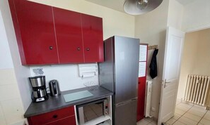 A compact kitchen with red cabinets, a stainless steel refrigerator, a microwave, and a coffee maker.