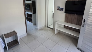 Ein modernes Zimmer mit Flachbildfernseher, integrierten Regalen, einem kleinen Tisch und einer Tür zu einem anderen Raum.