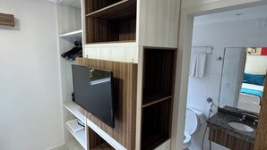 Ein Zimmer mit integriertem Fernseher, einer Holzregalanlage, einer Toilette und einem Badezimmer mit Waschbecken und Spiegel.