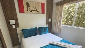 Ein Hotelzimmer mit einem Bett, einer Wand-Klimaanlage, einem Fenster mit Vorhängen und einem teilweisen Blick auf eine Tür.