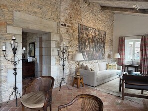 Une pièce avec un mur en pierre, un canapé blanc, une chaise en osier, une table en bois et un chandelier.