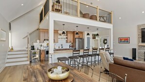 A spacious living area with a high ceiling, a dining table, a sofa, and a kitchen area with a balcony.