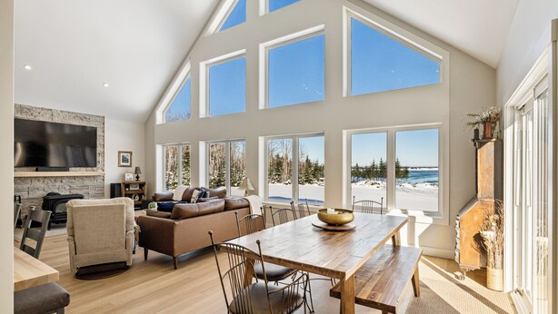 A spacious living area with a large wooden dining table, comfortable seating, a fireplace, and large windows offering a view of the outdoors.