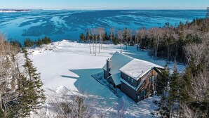 A cabin with a snow-covered roof, surrounded by a forest and a frozen lake.