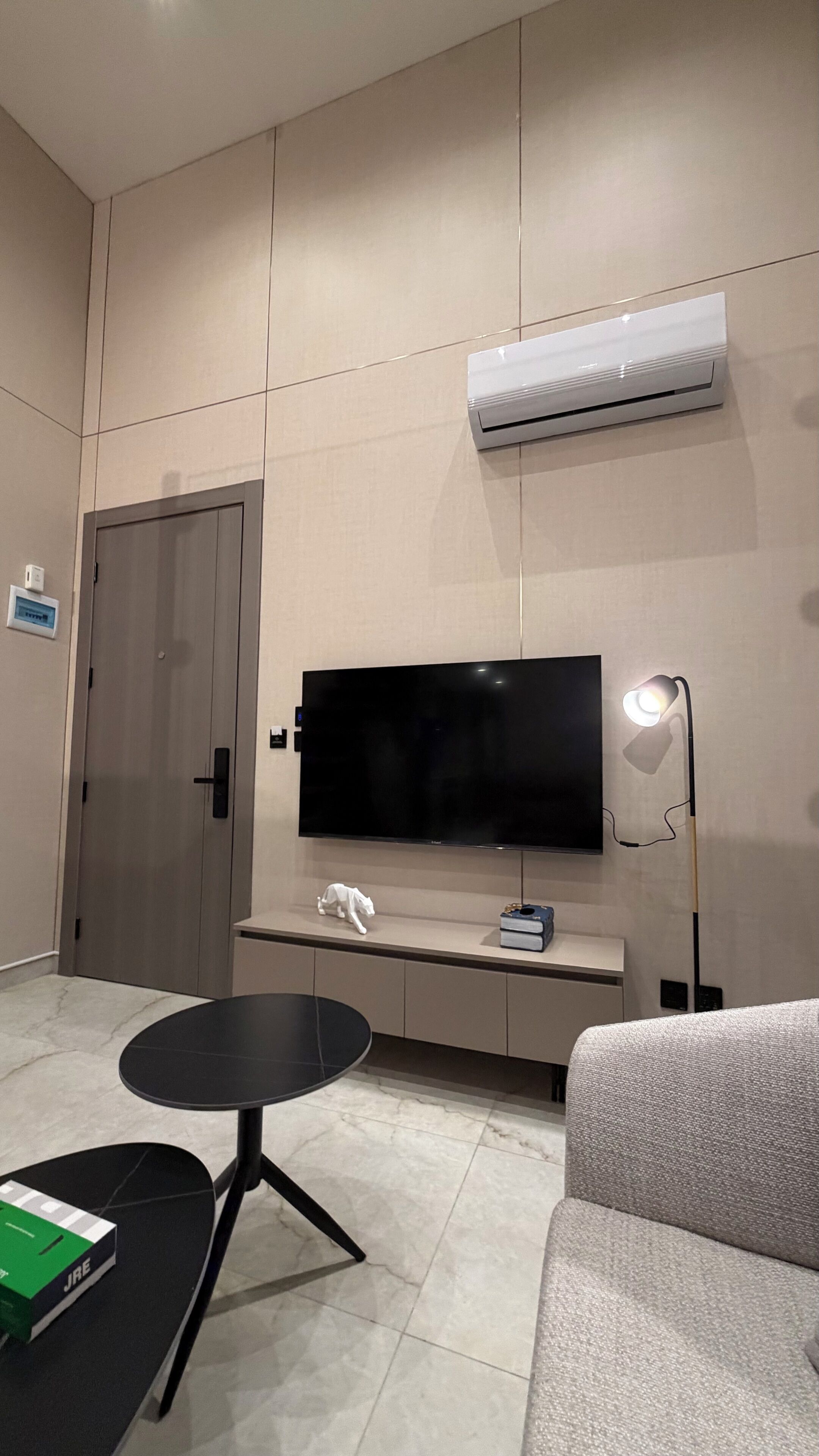 Un salon moderne avec un téléviseur à écran plat, un lampadaire, un canapé, une petite table ronde et une porte.