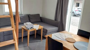 Ein modernes Zimmer mit einem grauen Sofa, einem Holztisch, einem kleinen Holzstuhl und einem Fenster mit Vorhängen.