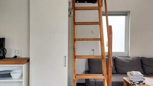 Ein Zimmer mit einer Holzleiter, einem Sofa, einem Tisch mit gefalteter Kleidung und einem Schrank mit Geschirr.