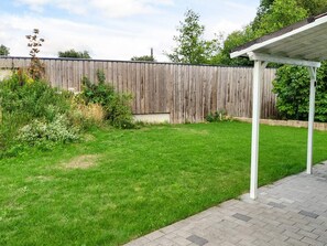 A backyard with a wooden fence, a grassy lawn, and a covered patio area. - 4 Person Holiday Home in Falkenberg (Falkenberg)