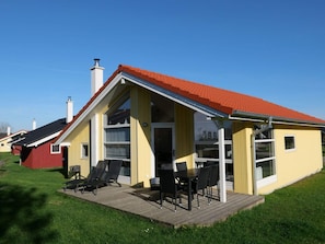 A yellow building with a red roof, large windows, and a wooden deck with outdoor furniture. - 4 Star Holiday Home in Grossenbrode (Grossenbrode)