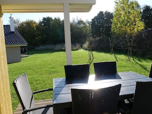 A patio with a table and chairs, a covered area, and a view of a grassy yard with trees. - 4 Star Holiday Home in Grossenbrode (Grossenbrode)