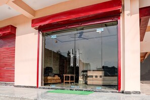 A modern building with a red awning, large glass entrance, and a small wooden stool outside. - Deluxe Super Collection O Salori (Chandpur)
