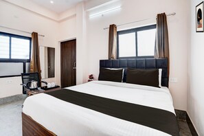 A hotel room with a bed, a desk with a kettle, a chair, a window with curtains, and a door. - Deluxe Super Collection O Salori (Chandpur)