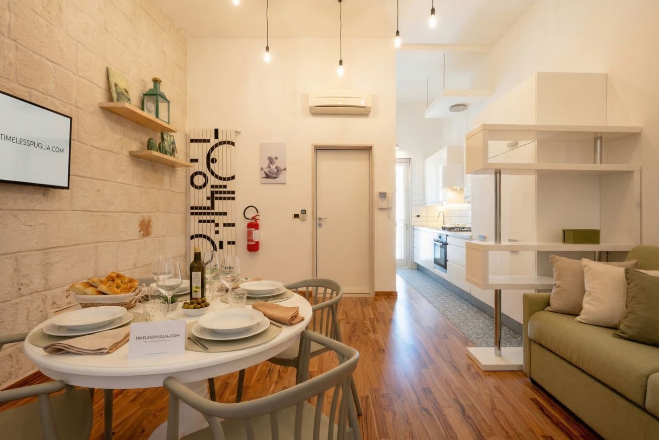 A dining area with a round table set for four, a whiteboard with text, and a kitchen in the background.