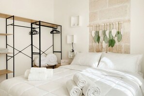 Ein Hotelzimmer mit einem Bett, einem Holzregal, einem Haken für Handtücher an der Wand, einer Wandleuchte und einer Wanddekoration.