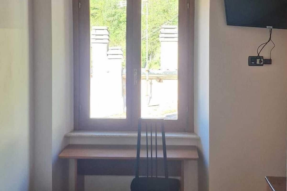Una habitación con cama, escritorio, silla, televisor montado en la pared y ventana con vista a zonas verdes.