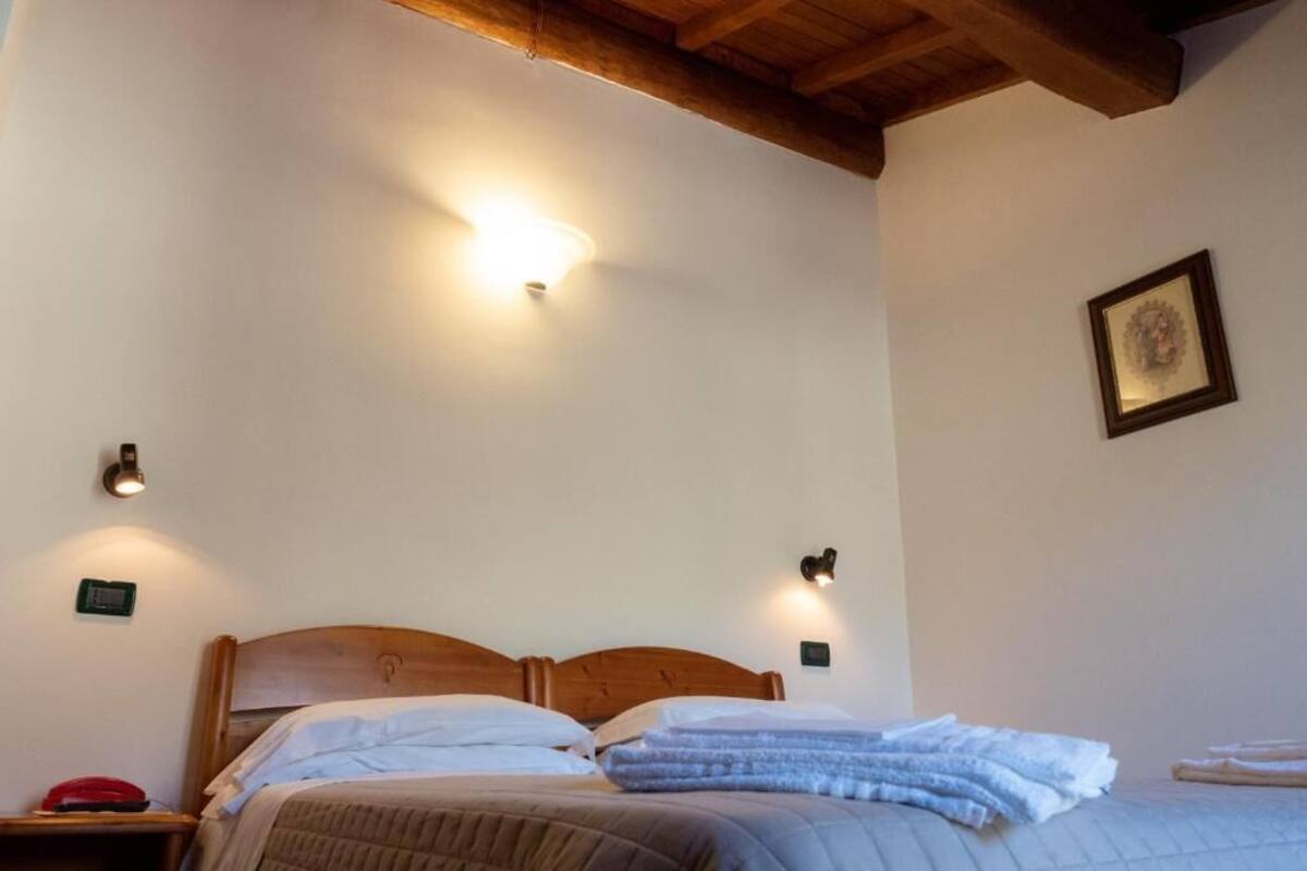 Un dormitorio con cabecera de madera, dos lámparas de noche, un cuadro en la pared y un teléfono rojo en la mesita de noche.