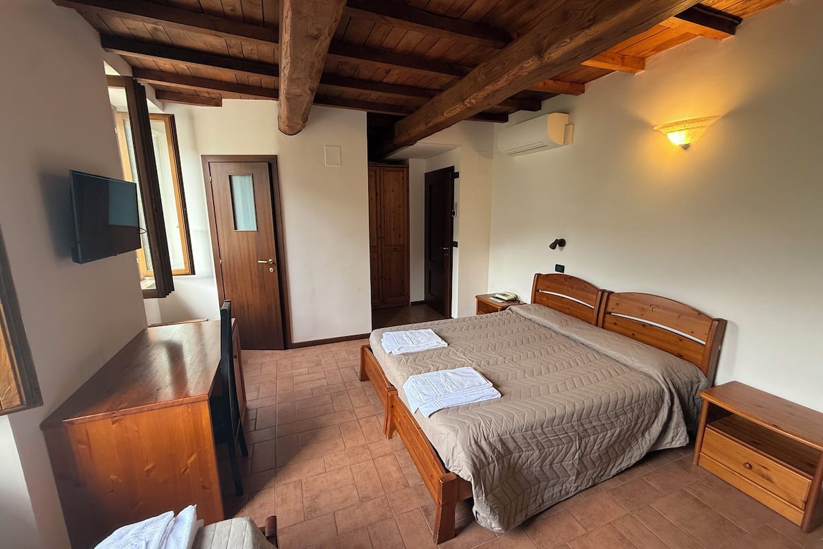 Un dormitorio con cama de madera, una mesita de noche, un escritorio con televisor de pantalla plana y una puerta que da a otra habitación.