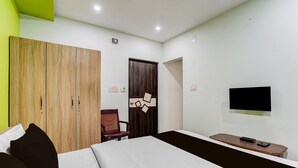 Habitación de hotel con una cama, un armario de madera, una silla, un escritorio con un control remoto y un televisor fijado a la pared.