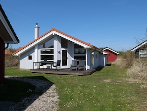 Ein eingeschossiges Haus mit Satteldach, Schornstein und einer Terrasse mit Gartenmöbeln.