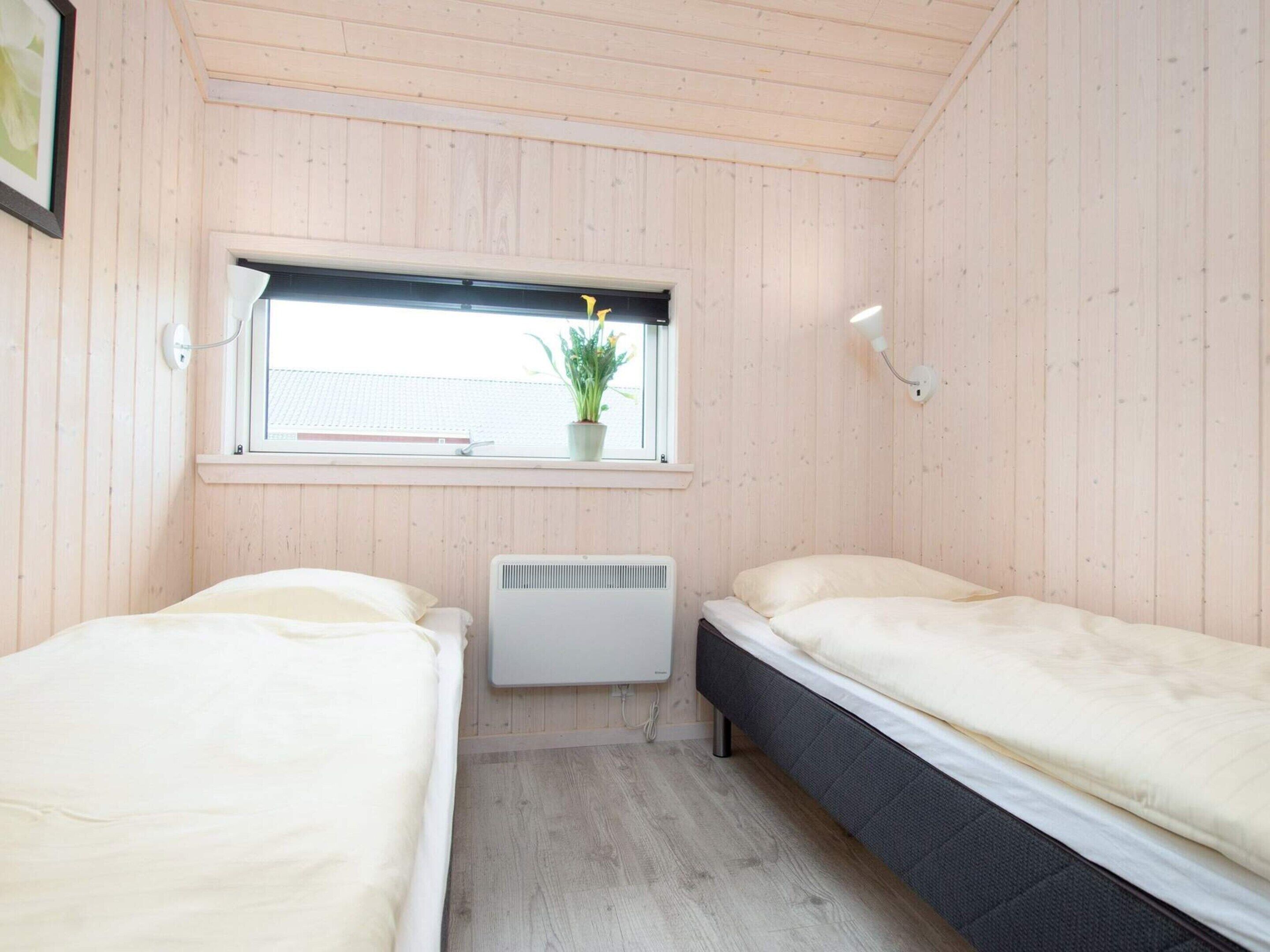 Een kamer met twee bedden, een raam met een plant, een radiator en een wandlamp.