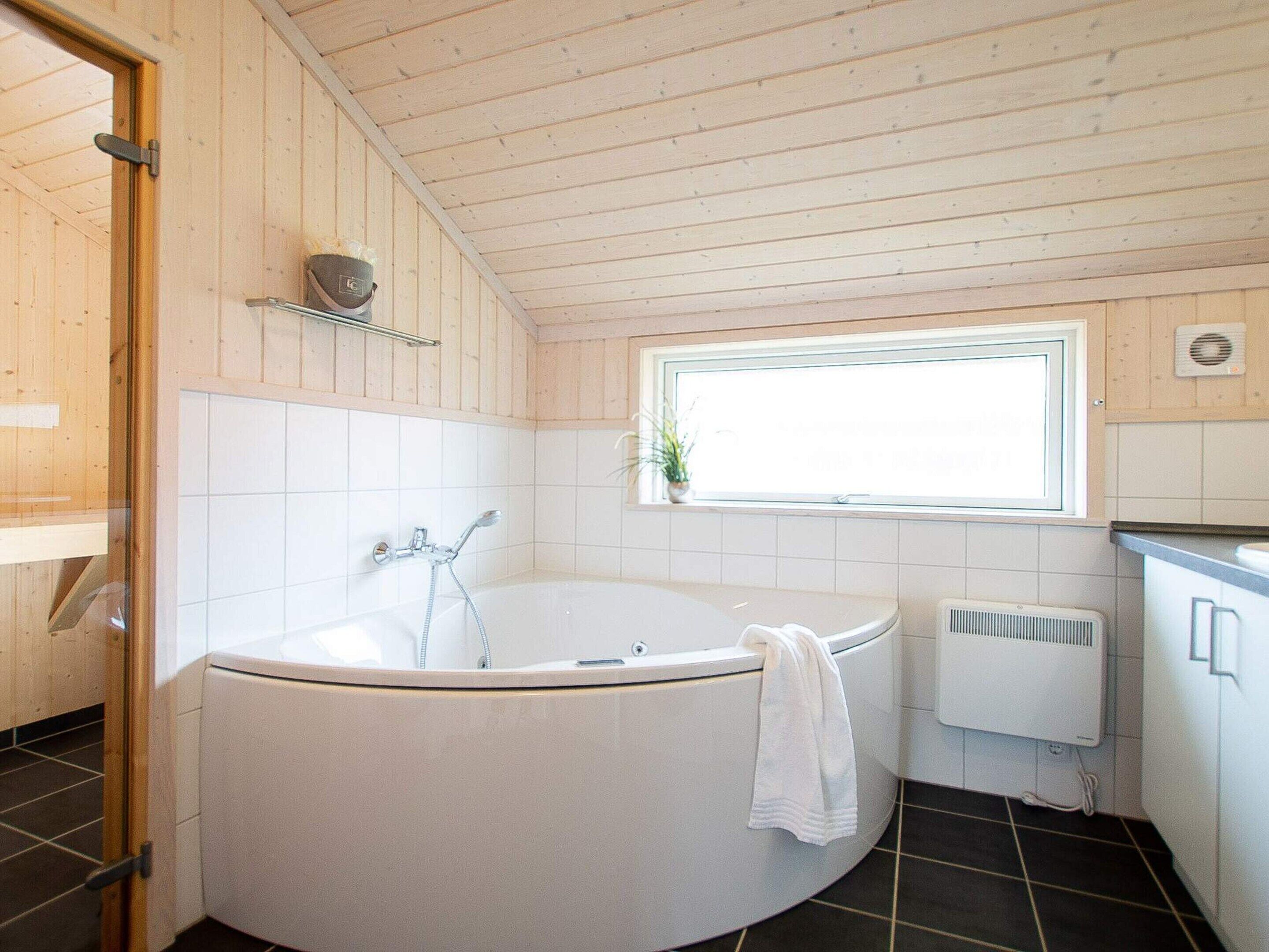A bathroom with a freestanding bathtub, a window, a radiator, and wooden paneling.