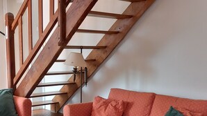 Ein Wohnzimmer mit einer Holztreppe, einem gemusterten Sofa, einem Couchtisch mit Kerzenhaltern und einem Teppich mit Muster.
