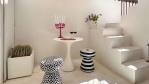 A modern interior with a white staircase, a round table with a candelabra, a polka-dotted stool, and a cactus in a planter. - Backhoe Suite (Taormina)
