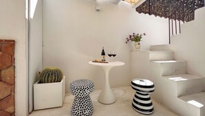 A patio with a white table, a cactus planter, a polka-dotted stool, a striped stool, and a staircase. - Backhoe Suite (Taormina)