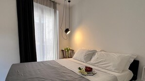 A neatly made bed with white linens, a bedside table with a vase of flowers, and a lamp. - Backhoe Suite (Taormina)