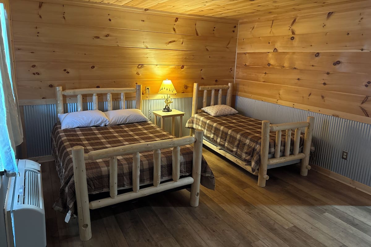 A cabin with two wooden beds, a small table with a lamp, and a heater.