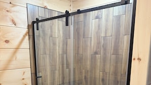 A shower enclosure with a wooden panel design, a glass door, and a tiled floor. - 4 Corners Event Center (Elk Falls)