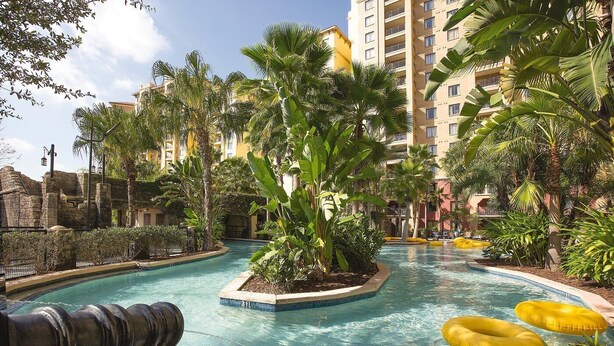 A swimming pool surrounded by tropical plants and a stone wall. - Wyndham Bonnet Creek, 3 bedroom deluxe suite, 3 BR/2 BA, kitchen, near EPCOT (Lake Buena Vista)