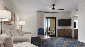 A hotel room with a sofa, a small table, a ceiling fan, a TV, and a view through a door. - Wyndham Bonnet Creek, 3 bedroom deluxe suite, 3 BR/2 BA, kitchen, near EPCOT (Lake Buena Vista)