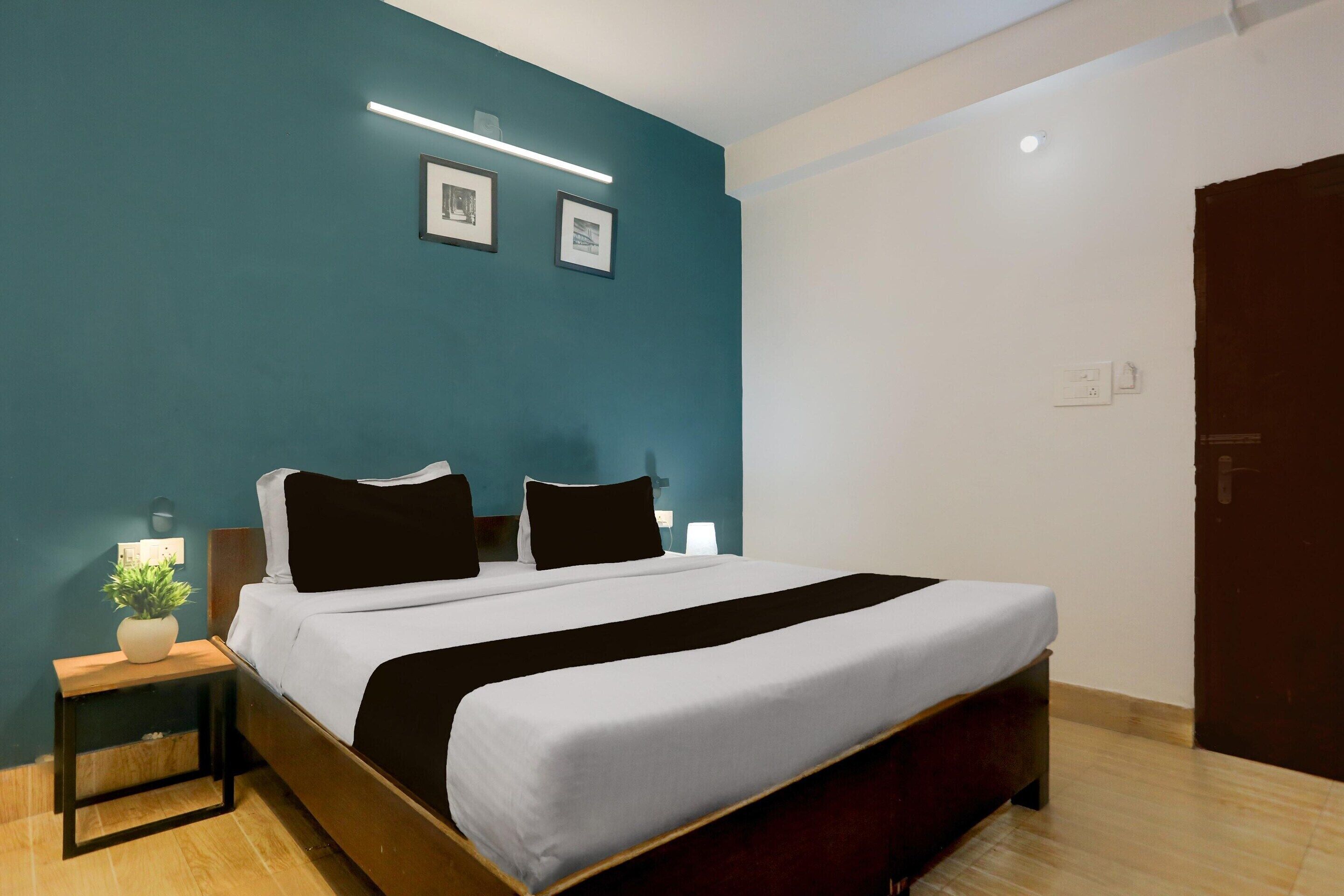 A bedroom with a bed, bedside tables, a nightstand, a wall-mounted light, and a door.