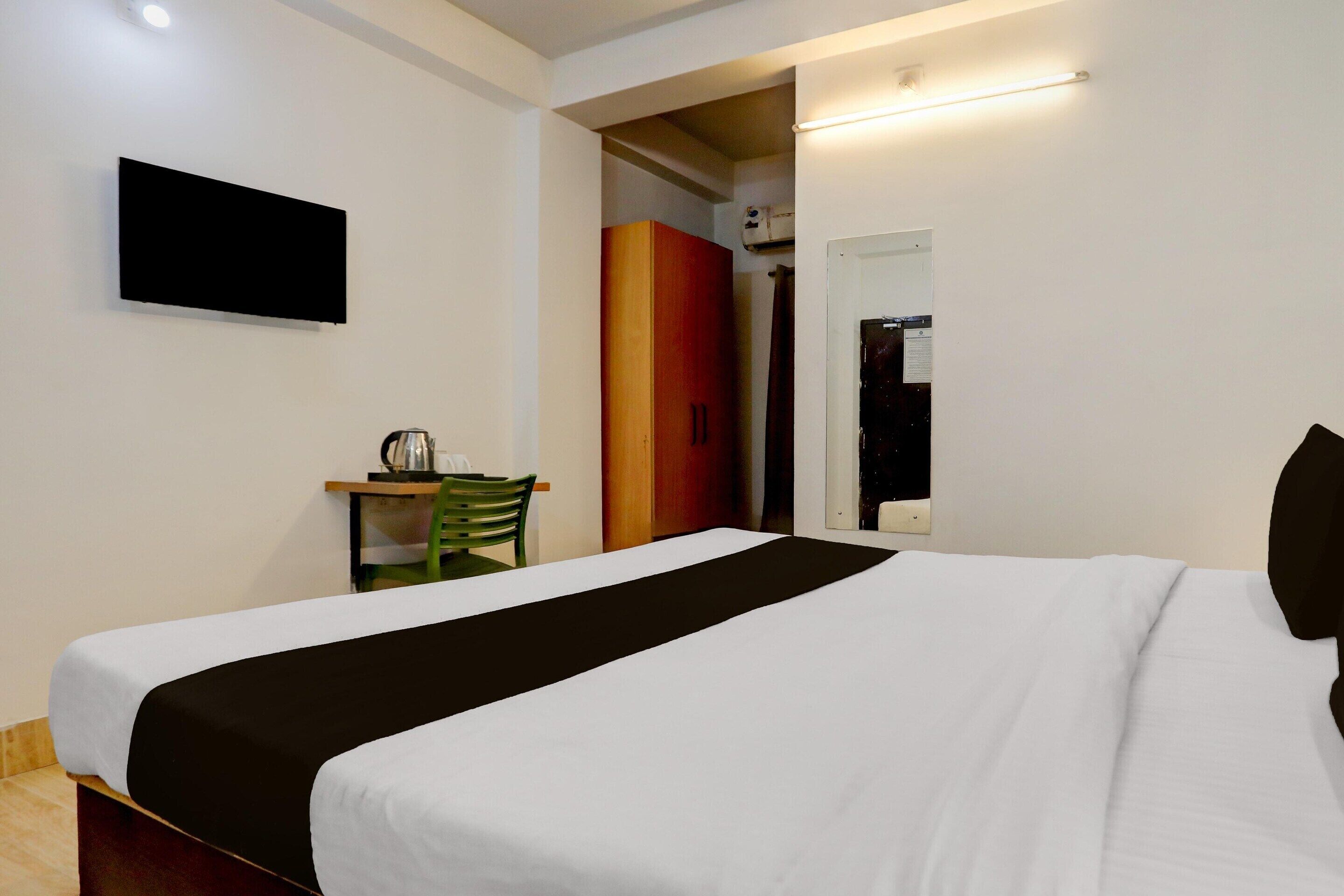 A hotel room with a bed, a TV mounted on the wall, a desk with a chair, and a wardrobe.