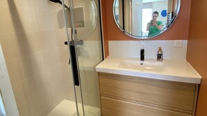 Ein Badezimmer mit Duschkabine aus Glas, einem runden Spiegel, einem weißen Waschbecken und Holzschränken.