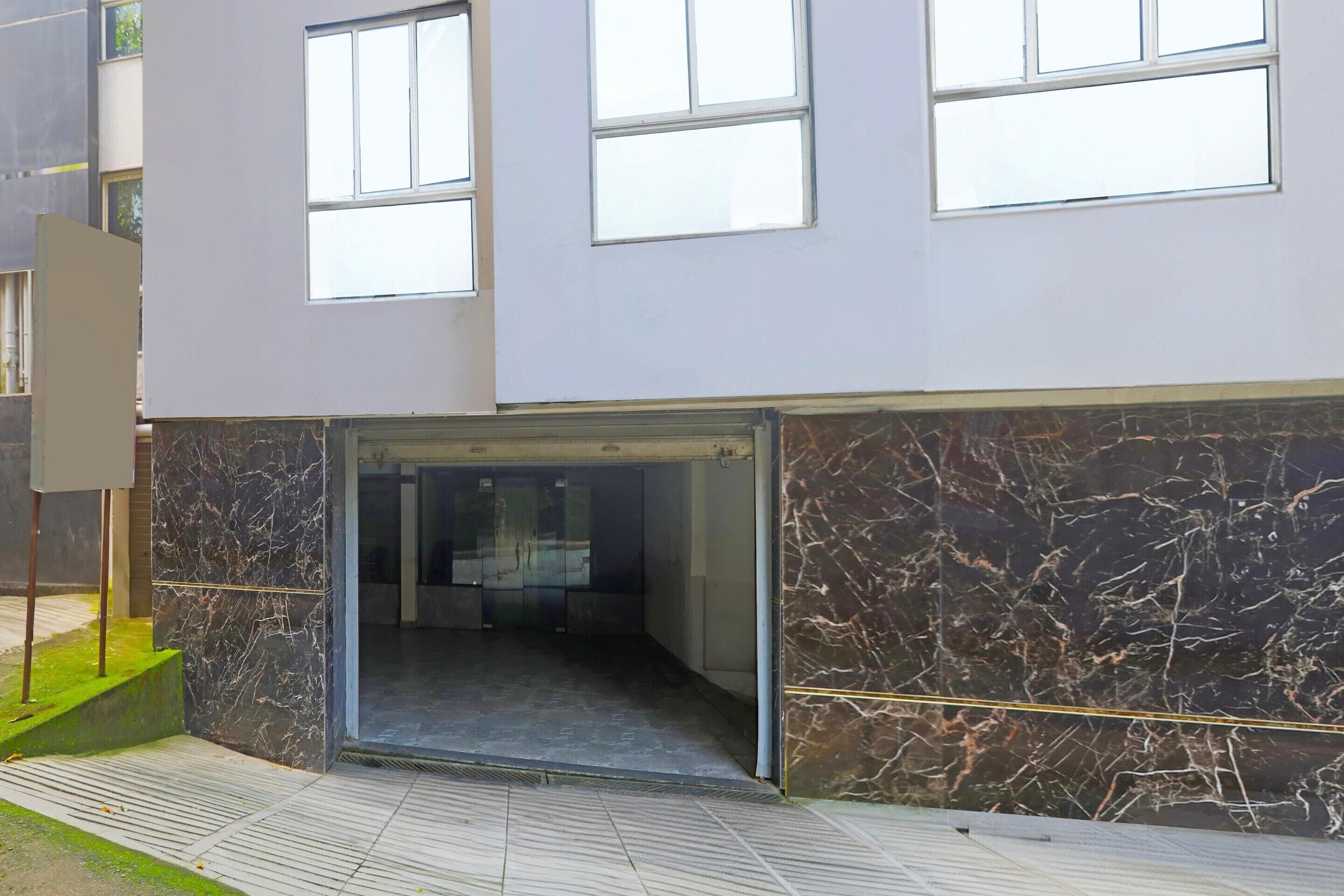 A modern building entrance with a glass door, a marble wall, and a tiled floor.
