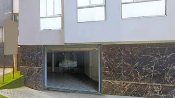 A modern building entrance with a glass door, a marble wall, and a tiled floor.