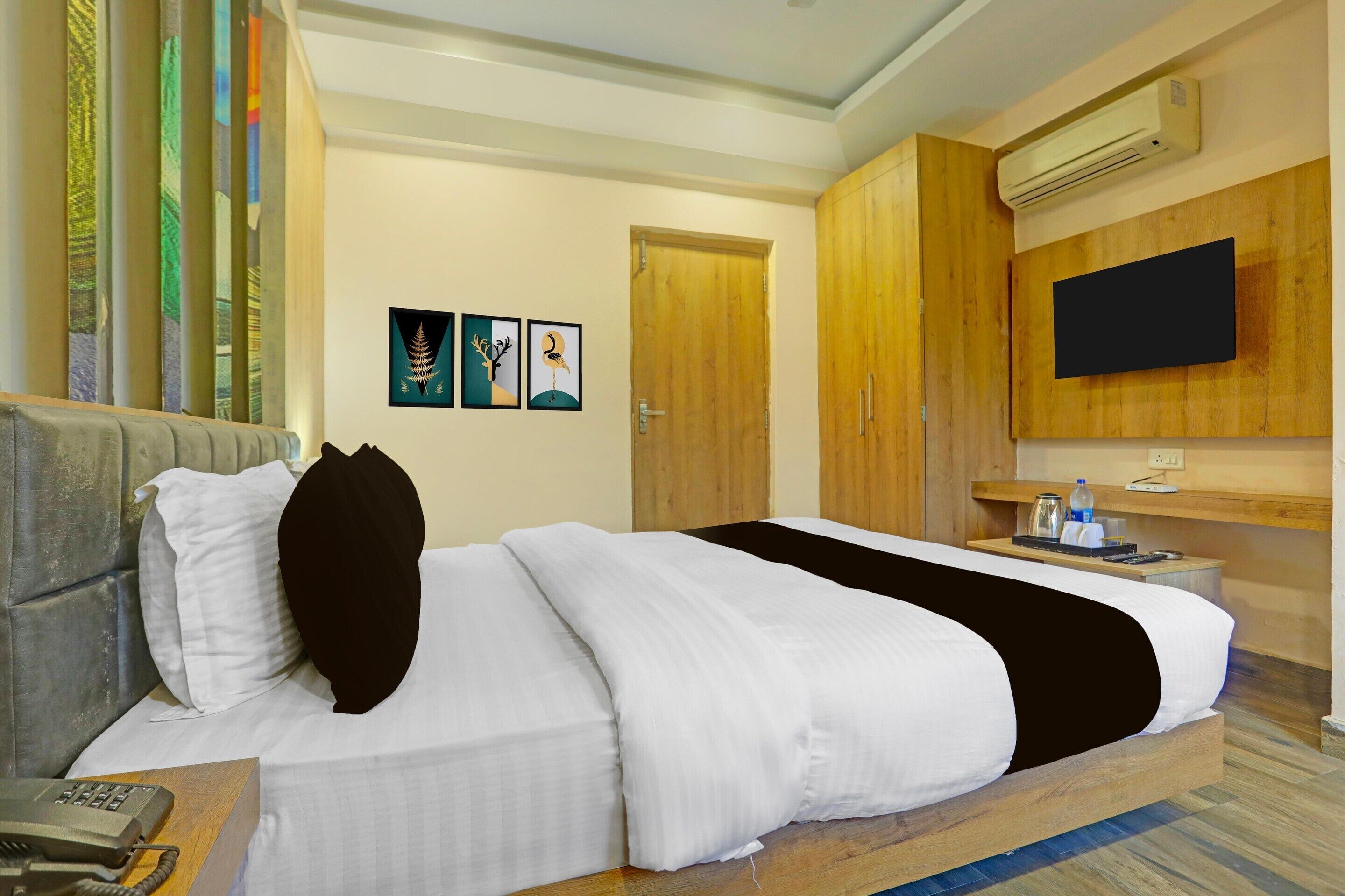 Una habitación de hotel con una cama, una mesita de noche con un teléfono, un televisor montado en la pared y obras de arte decorando la pared.