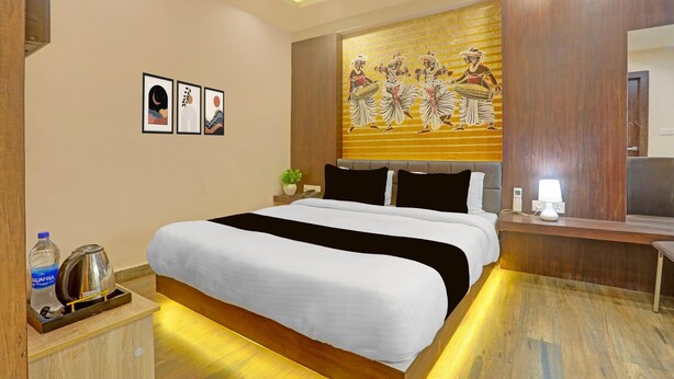 A hotel room with a bed, bedside table, wall art, and a mirror. - Super Deluxe Roomhotel Kuber Inn (Dhanbad)