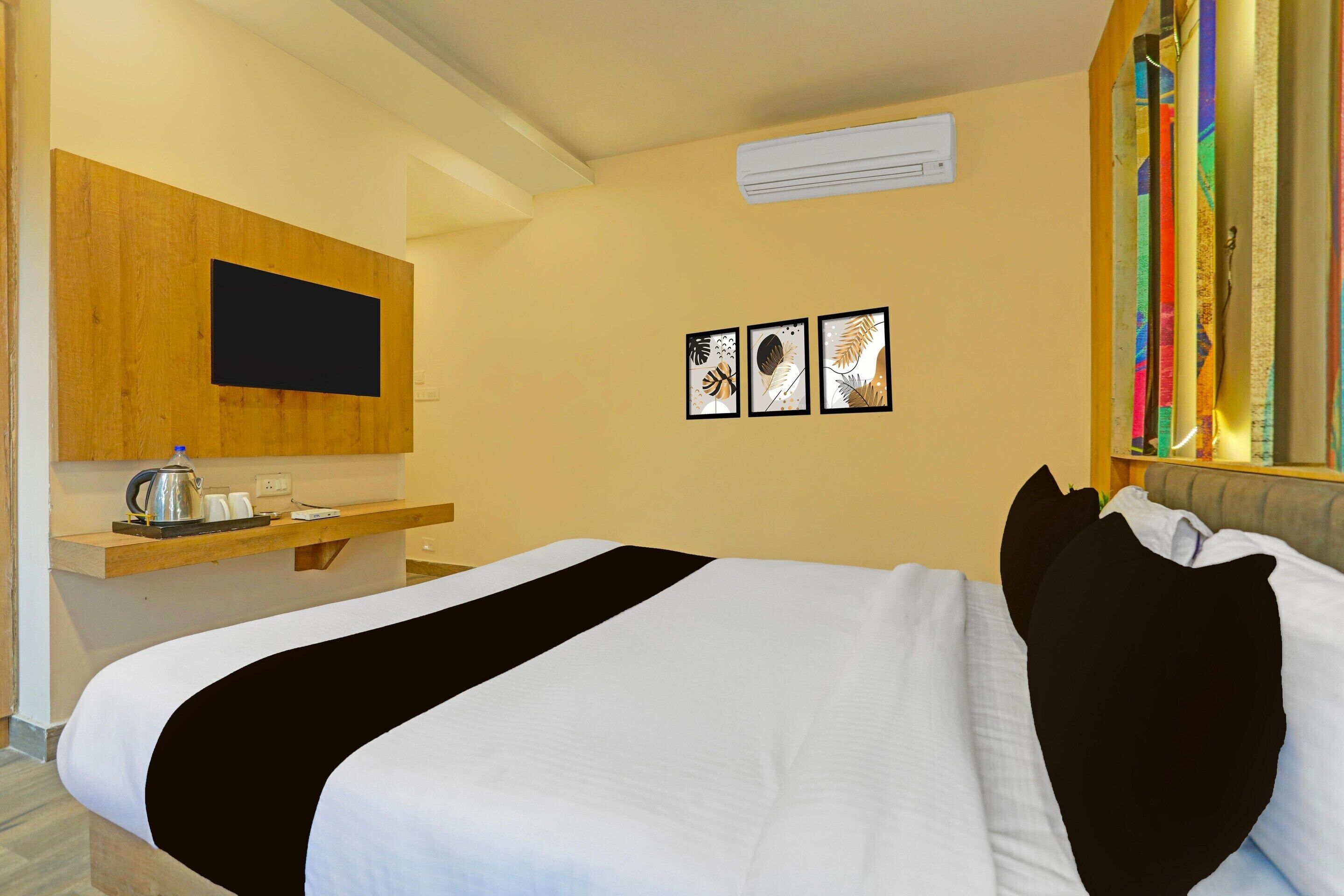 A hotel room with a bed, a wooden desk, a flat-screen TV, and three framed pictures on the wall.