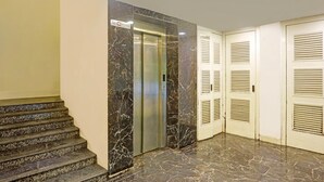 A marble-floored hallway with an elevator, a staircase, and a set of doors with louvered windows. - Super Deluxe Roomhotel Kuber Inn (Dhanbad)