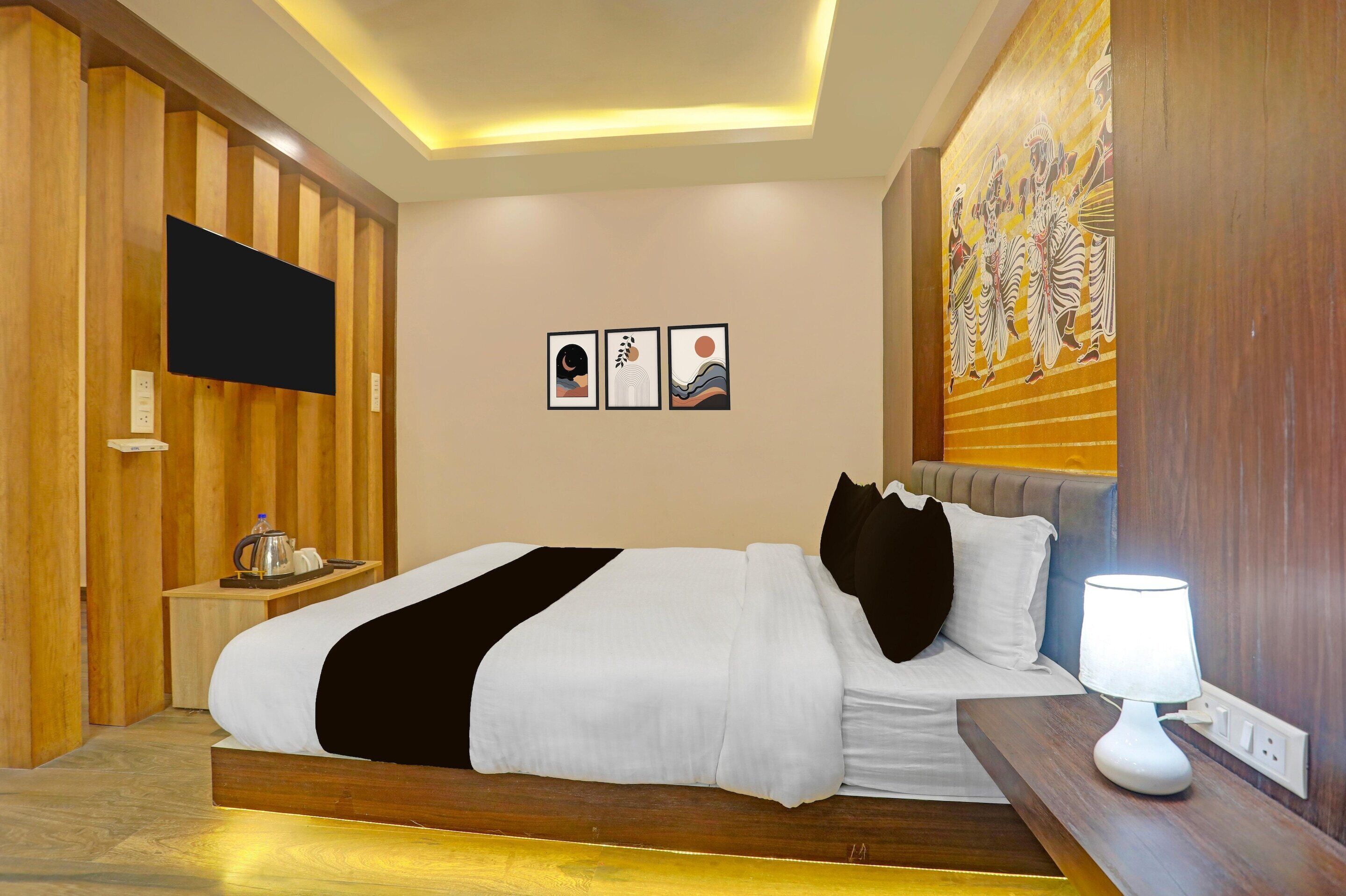 Una camera d'albergo con un letto, comodino, lampada, opere d'arte e televisore a parete.