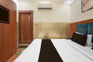 A hotel room with a bed, a TV, an air conditioner, and a door. - Deluxeramesh Palace (Prayagraj)