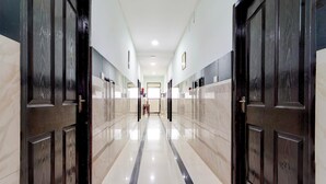 A hallway with dark wooden doors, a marble floor, and a view into a room with a bed and a window. - Deluxe Kakkanad Diamond (Kanayannur)
