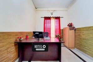 A reception desk with a sign reading 'HOTELO Company-Serviced,' a computer, a chair, a wooden cabinet, and a window with red curtains. - Deluxe Kakkanad Diamond (Kanayannur)
