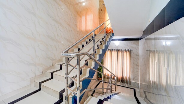 A modern interior with a marble staircase, metal railings, and a view of a cityscape through large windows. - Deluxe Kakkanad Diamond (Kanayannur)