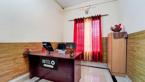 A hotel reception desk with a sign, a computer, a telephone, and a vase with flowers. - Deluxe Kakkanad Diamond (Kanayannur)